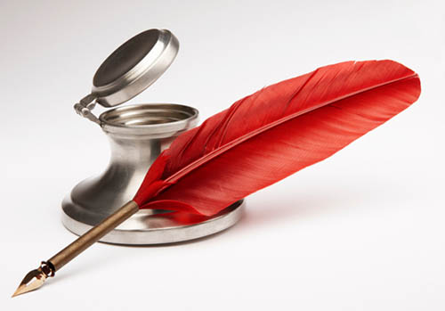 A red feather pen sitting next to an open inkwell.